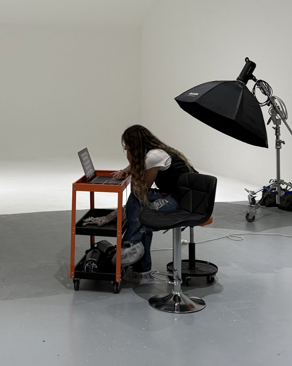 Isabella en el estudio, trabajando en la laptop sobre un carro naranja, junto a una luz de estudio